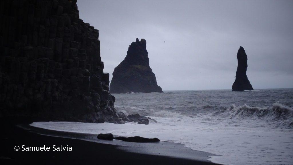 Vista dalla spiaggia di Reynisfjara sui faraglioni di Reynisdrangar. Sulla sinistra sorgono le colonne basaltiche di Hálsanefshellir e le omonime grotte.